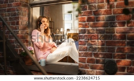 Beautiful Young Female Having a Call on her Smartphone While She Sits on her Windowsill. Expressive Woman Speaking on the Phone, Talking to her Long-Distance Partner on Sunday Evening. Royalty-Free Stock Photo #2238624715