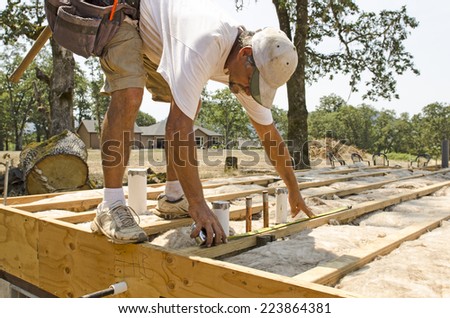 Framing contractor measuring for stubbed up domestic water and drain lines to install plywood subfloor to wood joist Royalty-Free Stock Photo #223864381