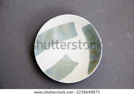 Top view of an empty white and blue ceramic pottery plate with glazed stroke, on a dark grey concrete background