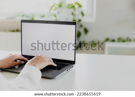 Woman hands typing on the laptop with empty blank white screen mockup. Computer is laying on the white table. Blurred background. Person working from home concept. Copy space area for text