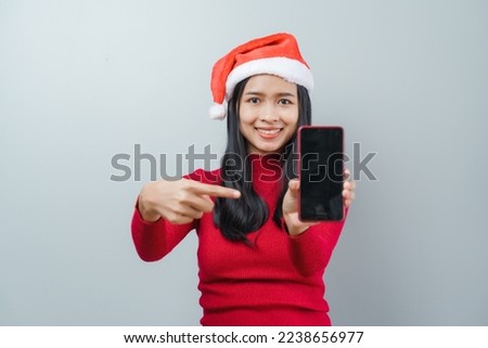 Pretty lovely lady asian thai women in red sweater and santa christmas hat isolated over grey background. Holding and using mobile smartphone or cellphone