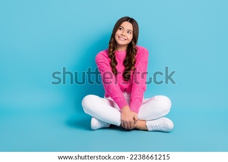 Full length photo of dreamy sweet lady wear pink sweater sitting legs crossed looking empty space isolated blue color background