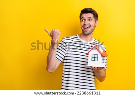 Photo of impressed funky man wear white t-shirt pointing looking empty space holding small house isolated yellow color background