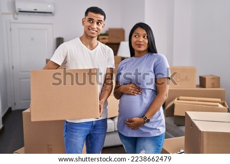 Young hispanic couple expecting a baby moving to a new home smiling looking to the side and staring away thinking. 