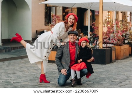 A stylish family of three strolls through the autumn city posing for a photographer . Dad, mom and daughter in the autumn city