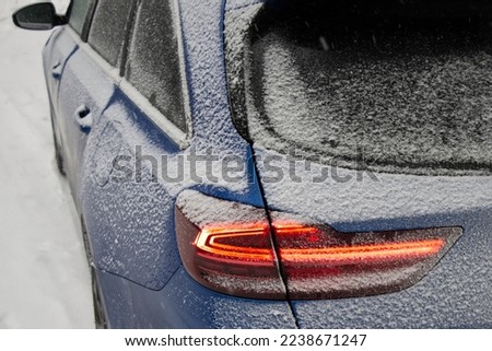 Parked cars on a winter day after a snowstorm. The back in the snow. Cars covered by deep snow. Backs, rear view. Details of back red lights.