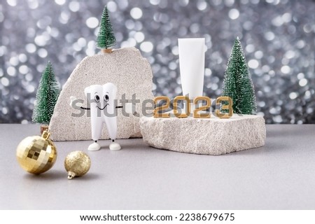 cartoon model of a tooth, the numbers 2023 and a tube of toothpaste on a podium made of stone and Christmas trees on a background of silver bokeh