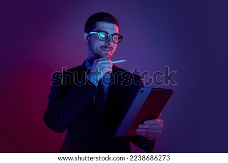 Young man, manager wearing business suit and eyeglasses using digital tablet on gradient blue purple background in neon light. Studying, online work, job, finance, new app concept Royalty-Free Stock Photo #2238686273