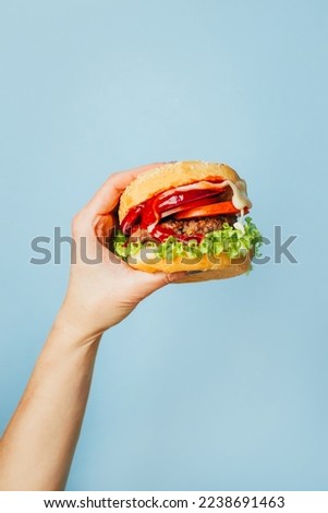 close-up on a hamburger in a female hand on a blue background Royalty-Free Stock Photo #2238691463