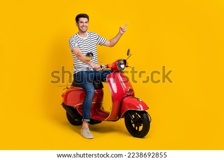 Full length photo of positive pretty guy dressed striped t-shirt riding moped pointing empty space isolated yellow color background Royalty-Free Stock Photo #2238692855