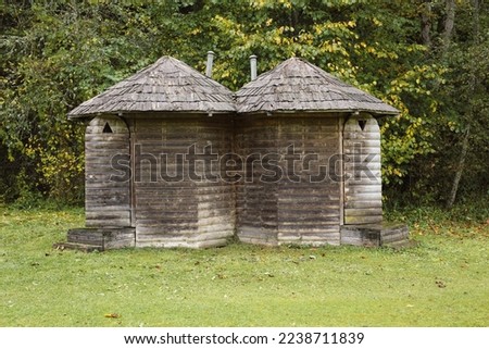 Two countryside outdoor wooden toilets, triangle sign, green grass