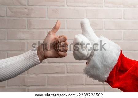 Santa and the girl give a thumbs up on the background of a light brick wall