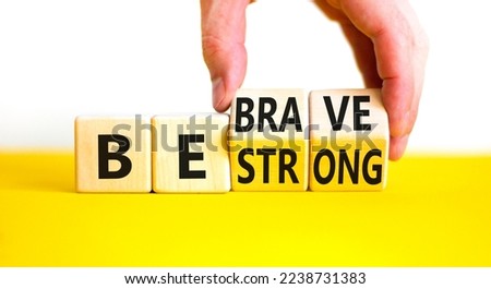 Be strong and brave symbol. Concept word Be strong Be brave on wooden cubes. Beautiful yellow table white background. Businessman hand. Business be strong and brave concept. Copy space.