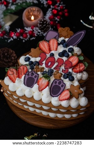 Christmas tree shaped new year honey ginger cake with whipped cream, strawberries, blueberries and rabbit decor. 2023 numbers. dark and moody food photography. Winter party