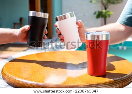 Hand cheering a thermal cup full of a beer. Pool Party. Stanley Classic Stay Chill Vacuum Insulated Pint Glass Tumbler, Stainless Steel Beer Mug with Built-in Bottle Opener, Double Wall Rugged Metal  Royalty-Free Stock Photo #2238765347