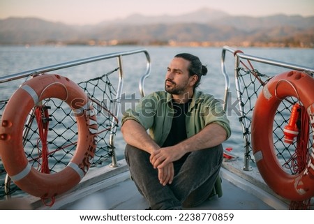 Portrait of a young man on a boat trip on a small ship in the sea on a sunny day. A Caucasian tourist guy in a summer shirt on the deck of a boat enjoys the wind in his face at sunset Royalty-Free Stock Photo #2238770859