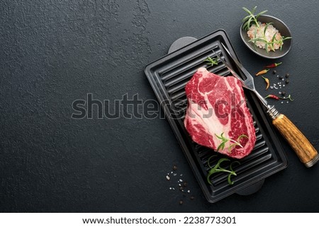 Raw beef steak. Raw fresh Chuck roll steak with rosemary, salt and pepper on cutting board on dark concrete background. Raw beef steak and spices for cooking. Royalty-Free Stock Photo #2238773301