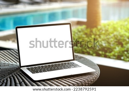 Laptop with blank screen for creative design on the table nearby pool with sun ray effect. Computer notebook with monitor clipping path for present landing page. Laptop computer mock up template