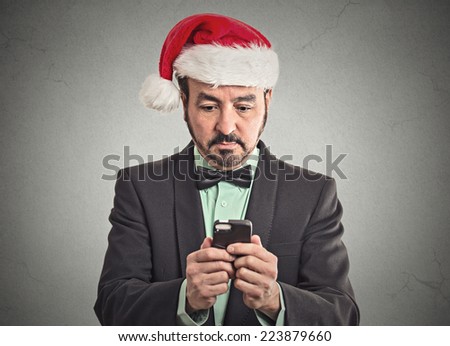 Portrait business man wearing red santa claus hat looking at smartphone searching online holiday season deal sale. Emotion facial expression body language. New technology convenience concept