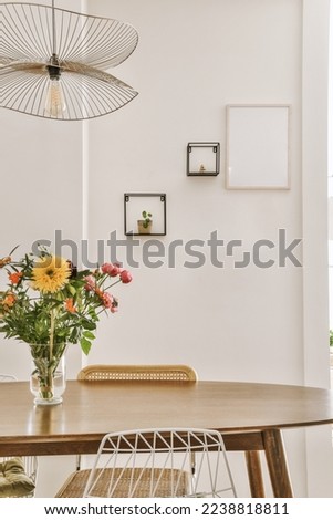flowers in a vase sitting on a wooden table next to a white wall with black framed pictures hanging above it