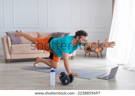 Photo of a middle aged man during online Pilates workout at home. Balance exercise. Healthy lifestyle concept.