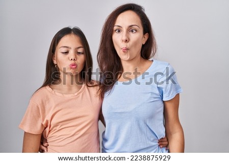 Young mother and daughter standing over white background making fish face with lips, crazy and comical gesture. funny expression. 