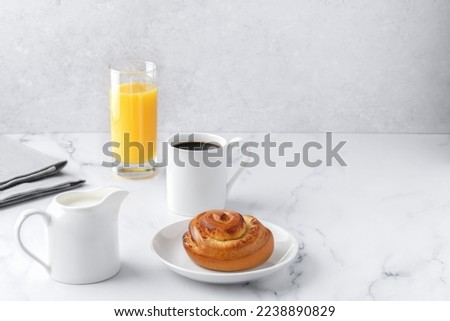 Swedish balanced lifestyle concept, Lagom. Cozy morning, with cup of coffee, homemade bun on the plate, milkman, glass of orange juice, table-napkin on a marble table. Horizontal, copy space.