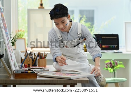Handsome male painter creates pictures, drawing with paints on canvas in art studio. Leisure activity, creative hobby and art concept