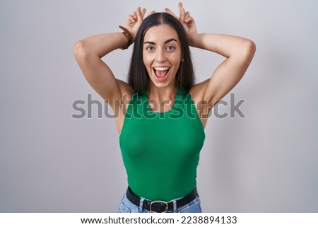 Young woman standing over isolated background posing funny and crazy with fingers on head as bunny ears, smiling cheerful 