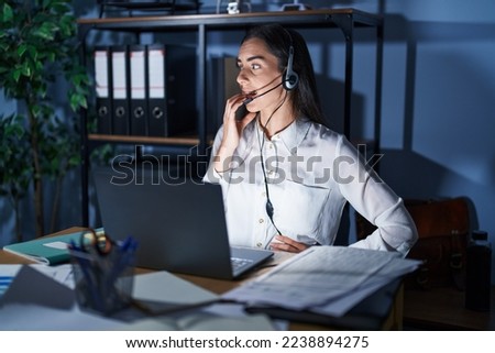 Young brunette woman wearing call center agent headset working late at night looking stressed and nervous with hands on mouth biting nails. anxiety problem. 