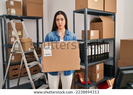 Hispanic woman working at small business ecommerce holding box skeptic and nervous, frowning upset because of problem. negative person. 
