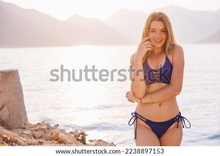 Slim beautiful blonde-haired woman with long hair wearing beach bikini in the sea on seascape background.