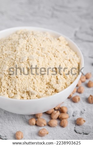Chickpea flour in bowl and seeds on light grey textured table, closeup