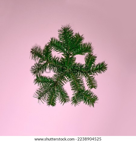 Christmas composition. Snowflake made of pine tree branches on pink table background. Flat lay, top view, copy space. Happy New Year card. Pink Christmas. Winter magic.