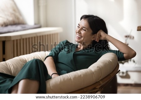 Cheerful beautiful young homeowner woman resting in soft stylish armchair, leaning head, looking away, thinking, smiling, laughing, having fun, enjoying leisure, comfort at home Royalty-Free Stock Photo #2238906709
