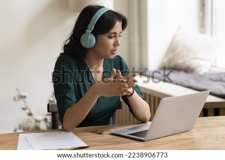 Serious Asian freelance worker woman in trendy wireless headphones talking on video call, using laptop computer for online business communication with client, speaking on Internet conference Royalty-Free Stock Photo #2238906773