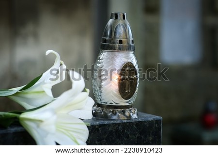 Lilies and grave lantern with burning candle on tombstone in cemetery, space for text