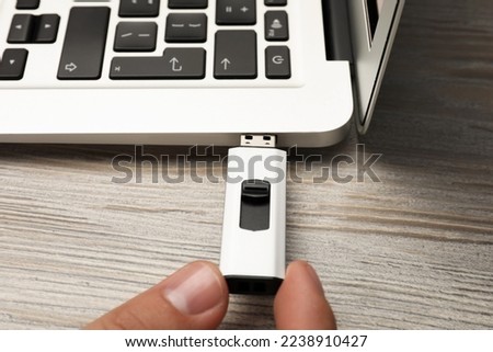 Man connecting usb flash drive to laptop at white wooden table, closeup