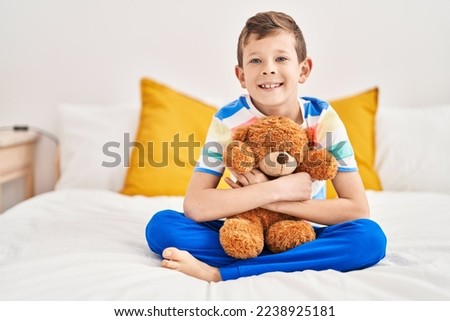 Blond child hugging teddy bear sitting on bed at bedroom Royalty-Free Stock Photo #2238925181