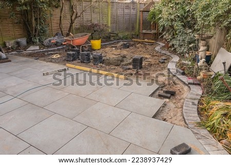 Garden paving under construction, with grey porcelain patio tiles and curved charcoal edge bricks. Royalty-Free Stock Photo #2238937429