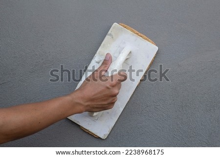 Hand of construction worker holding plastering trowel and sponge for using to smooth the walls in construction house site. Royalty-Free Stock Photo #2238968175