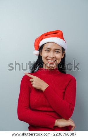 Pretty lovely lady asian thai women in red sweater and santa christmas hat isolated over grey background. hands pointing