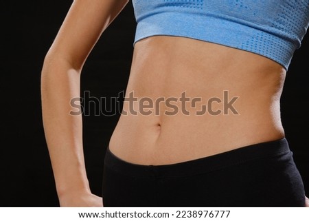 slim muscular woman in sportswear posing in studio on black background