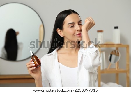 Young woman smelling essential oil on wrist indoors Royalty-Free Stock Photo #2238997915