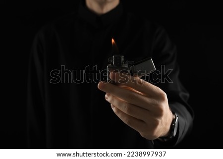 Man holding lighter with burning flame on black background, closeup. Space for text