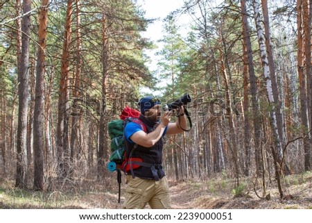 Photo of an ornithologist mith a camera walks through the forest and make a pics of the birds.