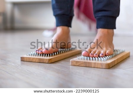 Photo of a female feet stand on a board with sharp nails over white background. Sadhu's board - practice yoga. Pain, trials, health, relaxation, cognition. Selective focus.