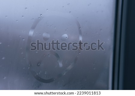 Unhappy, sad emoji on foggy glass window. Face sign close-up. Selective focus on photo. Depression and sadness concept.