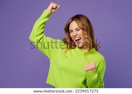 Young woman 30s she wearing casual green knitted sweater doing winner gesture celebrate clenching fists say yes isolated on plain pastel purple background studio portrait. People lifestyle concept Royalty-Free Stock Photo #2239017275
