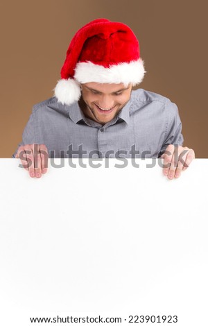 young man looking down on blank panel isolated on brown background. Smiling male looking down and wearing red hat